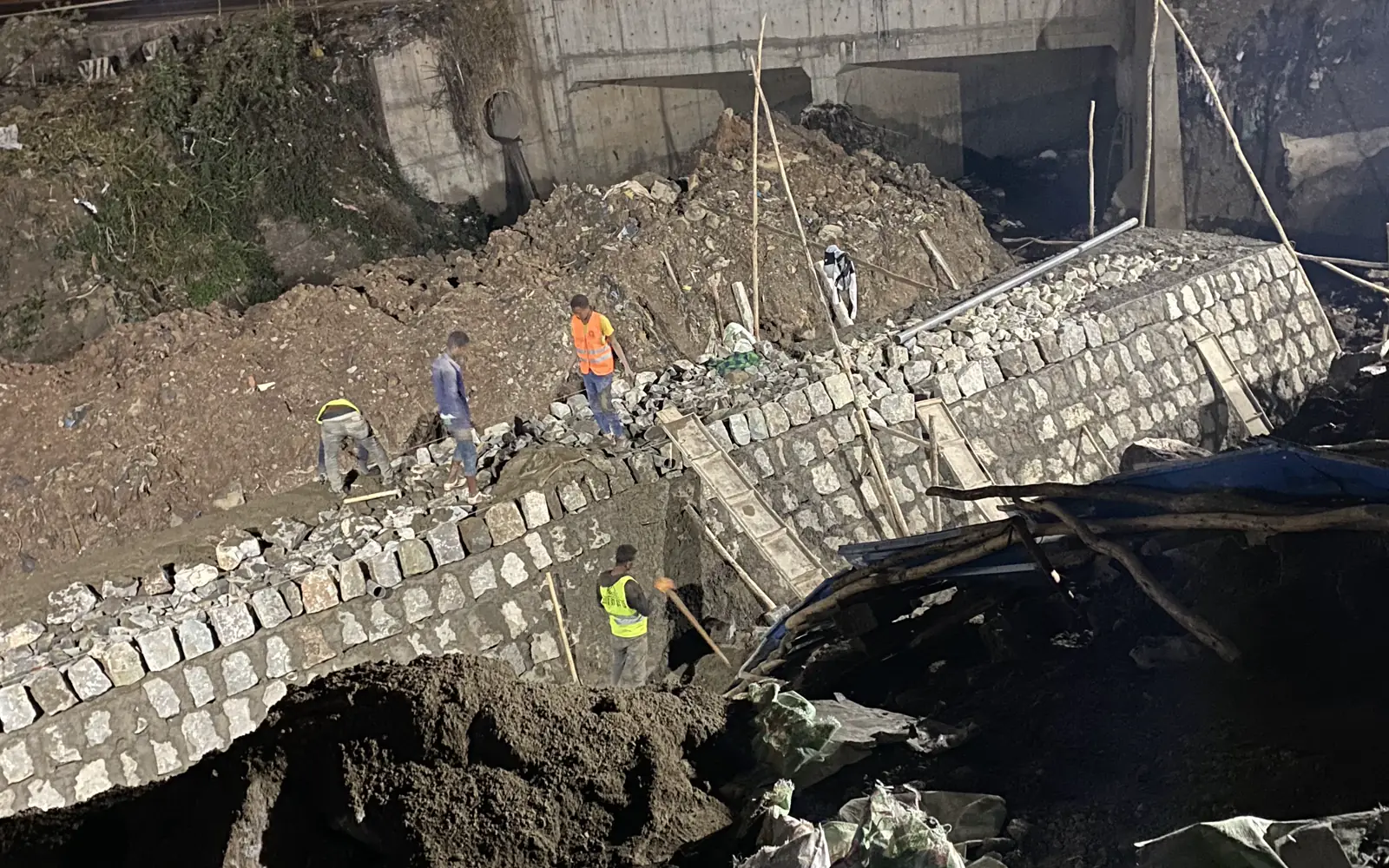 Stone retaining wall construction progressing beside an existing concrete structure
